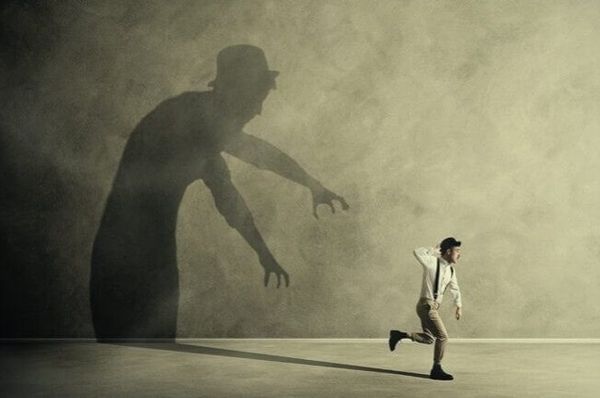 Small running figure moves away from a large reaching shadow on a wall
