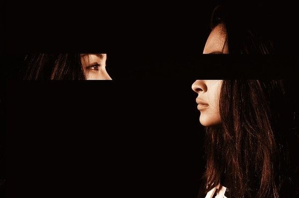 Two faces appear through narrow openings in a dark composition