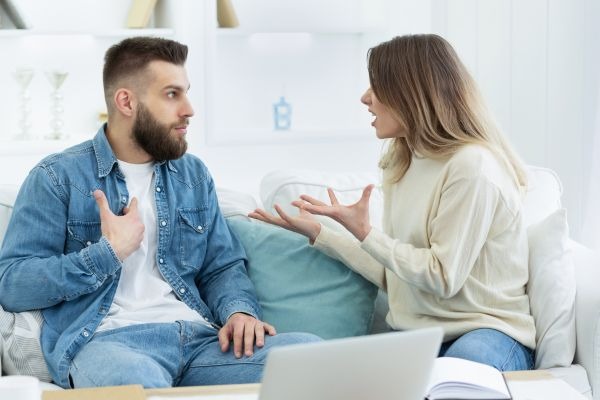 Two adults gesture during a conversation while seated on a sofa