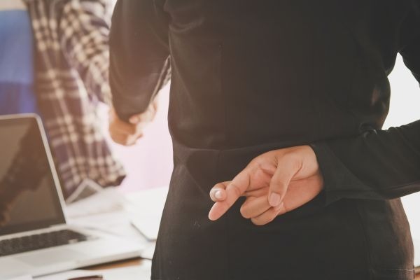 Person crosses their fingers behind their back while holding another hand