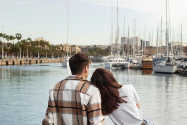 Two people sitting by a marina, one resting their head on the other's shoulder