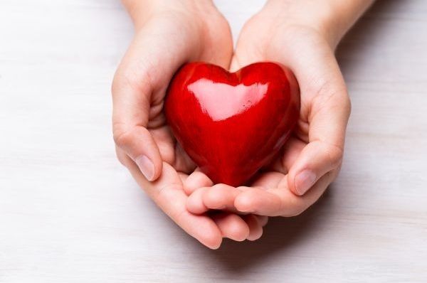 Two pairs of hands cradle a glossy heart-shaped object on a white surface