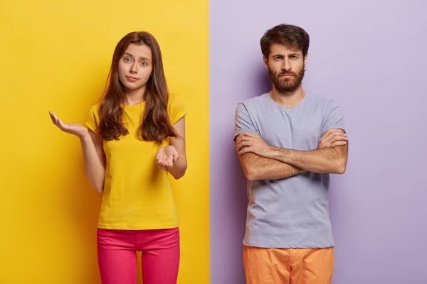 Two adults stand apart, one shrugging and the other with arms crossed