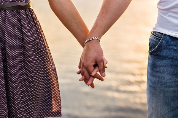 Two people holding hands outdoors beside a softly blurred shoreline