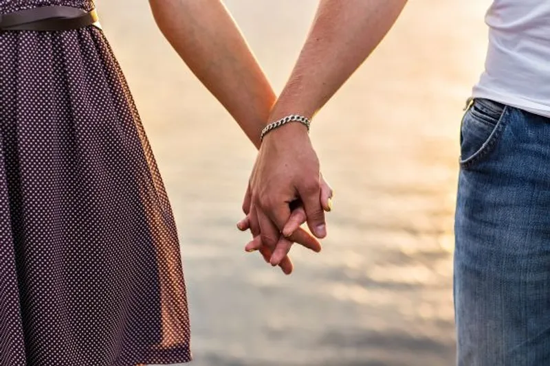 Two people holding hands outdoors beside a softly blurred shoreline