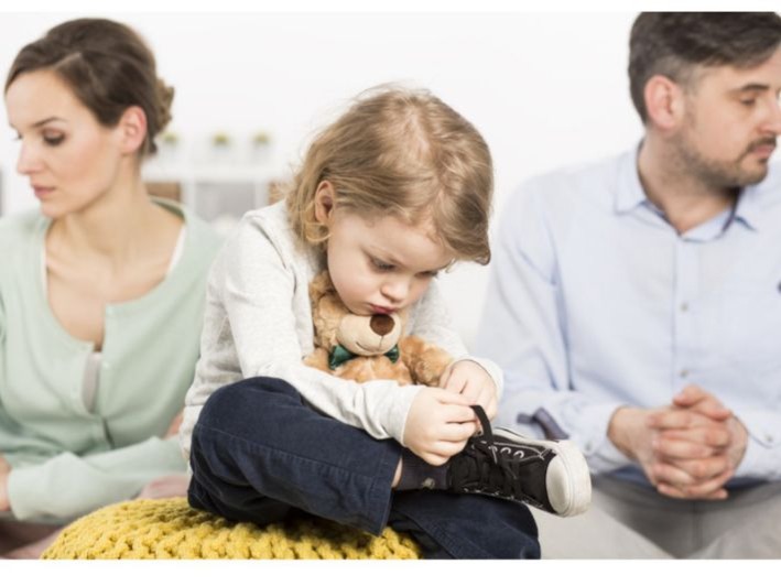 Child holds a sneaker's laces while two adults sit apart behind them