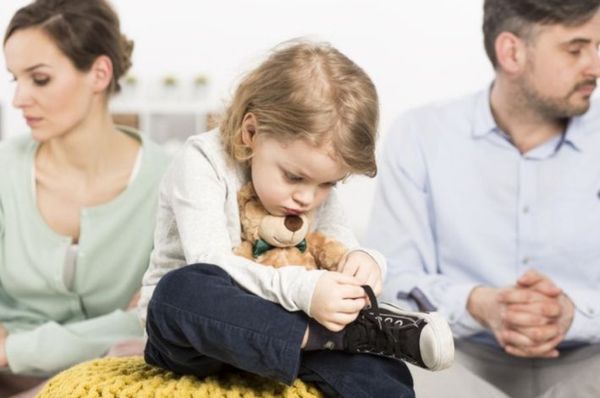 Child holds a sneaker's laces while two adults sit apart behind them