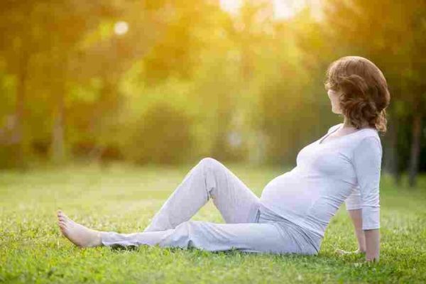 Pregnant person seated on grass in a sunlit park