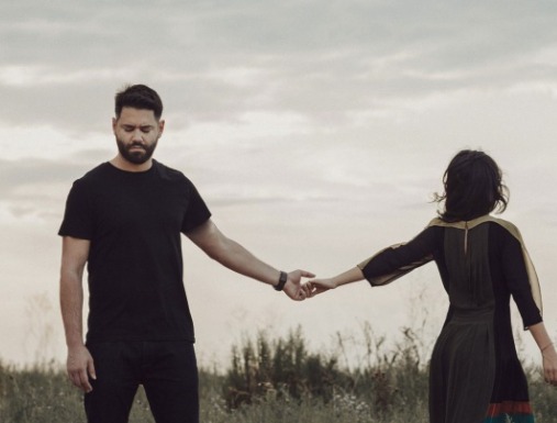 Two people standing apart and touching fingertips in an open field