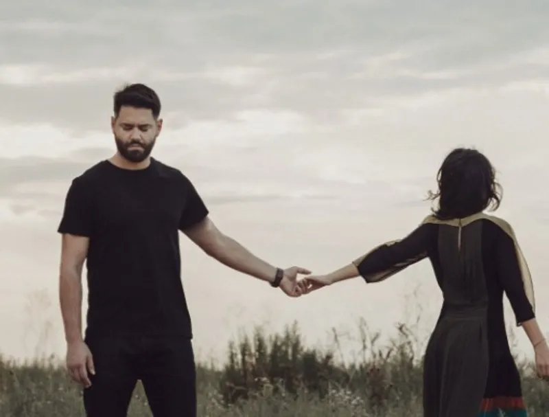 Two people standing apart and touching fingertips in an open field