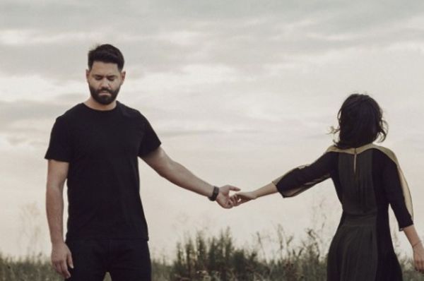 Two people standing apart and touching fingertips in an open field