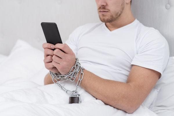 Person in bed holding a smartphone with chained wrists and a padlock