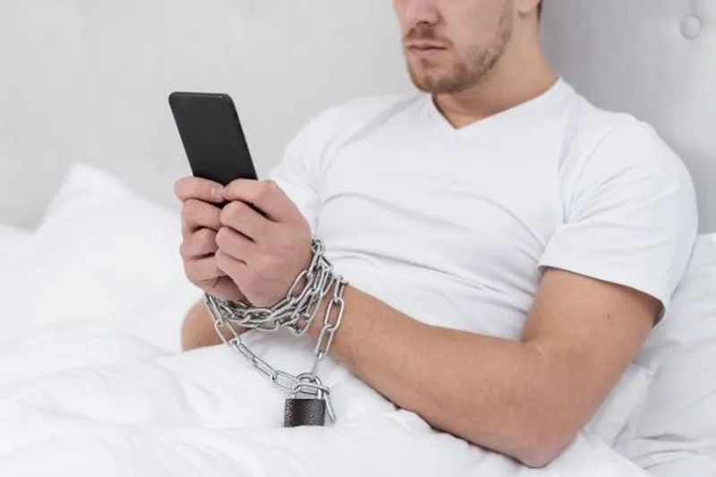Person in bed holding a smartphone with chained wrists and a padlock