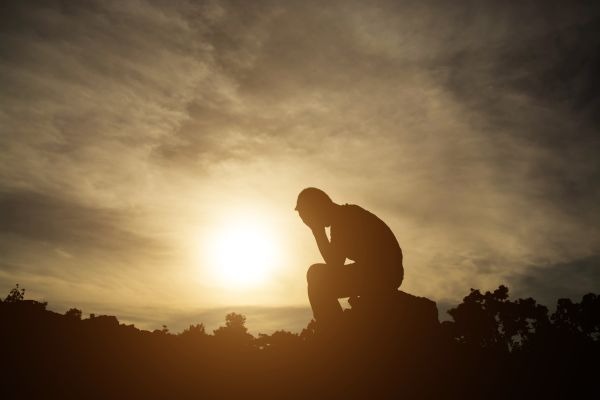 Silhouetted person sitting with a hand to their face against a low sun