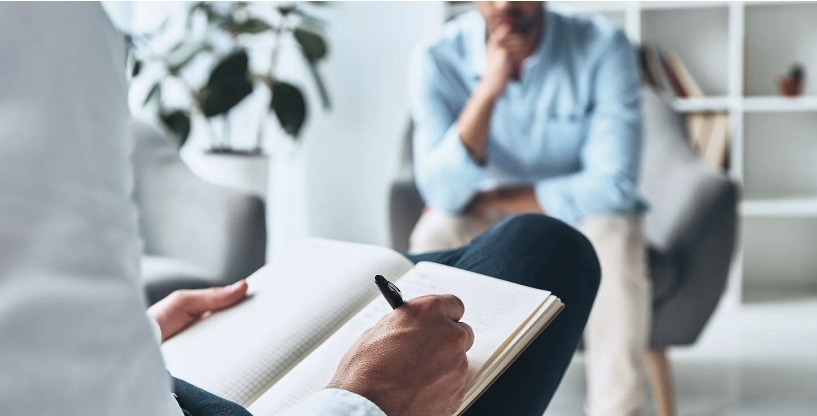 Seated person writes in a notebook while another person sits nearby