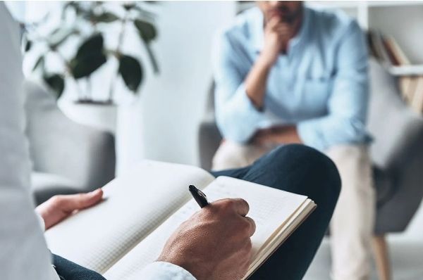 Seated person writes in a notebook while another person sits nearby