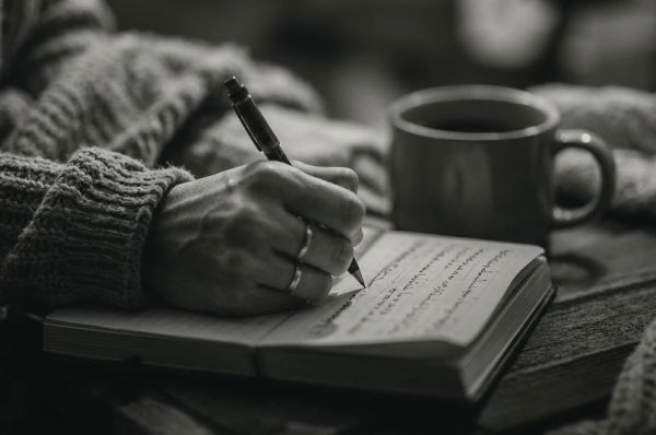 Close-up of a hand writing in a notebook beside a coffee cup, soft cozy lighting.