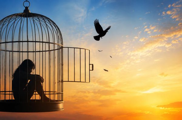 Silhouette in open cage at sunset, bird flying free, symbolizing escape and healing
