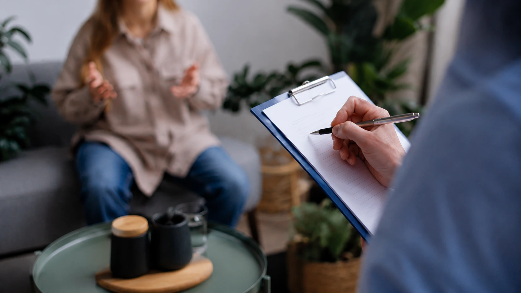 Therapist writing notes on clipboard while client speaks in a calm counseling session