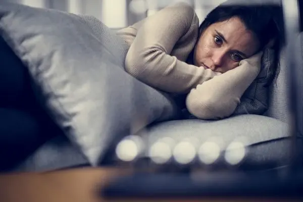Person curled up on a sofa, resting their head on folded arms