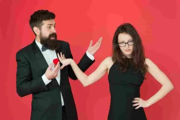 Bearded person holds out a small red box while another gestures away