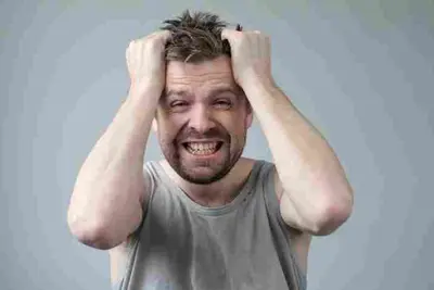 Person grips their hair with both hands while baring their teeth