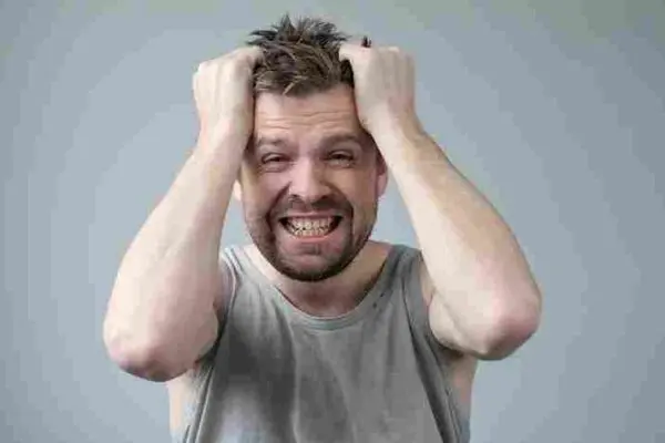 Person grips their hair with both hands while baring their teeth