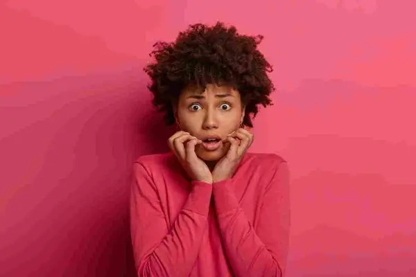 Person with wide eyes and hands raised near an open mouth against a plain wall