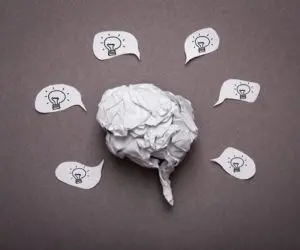 Crumpled paper shaped like a brain surrounded by speech bubbles with light bulbs