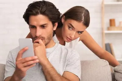 One person looks at a phone while another leans over their shoulder