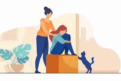 One person rests a hand on another seated on a box, with a cat nearby