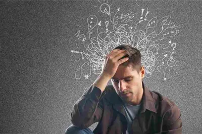 Seated person rests a hand on their head beneath tangled chalk lines and question marks