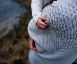 Hands resting on a rounded abdomen beneath a knitted sweater