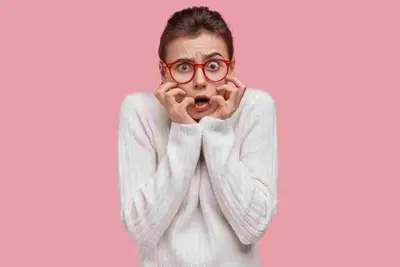 Person in red glasses holding their hands to their mouth against a pink background
