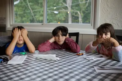 Three children at a table cover their eyes, ears, and mouth