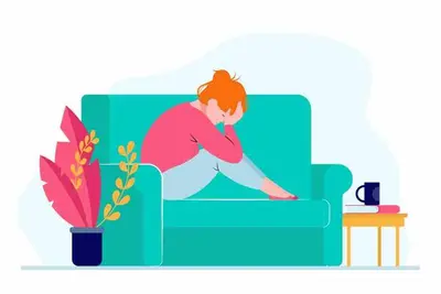 Person sitting curled up on a sofa with their head resting in one hand