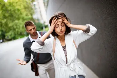 A person holds their head while another gestures behind them on a sidewalk