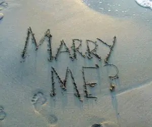 Marry me? traced in wet sand beside foamy seawater