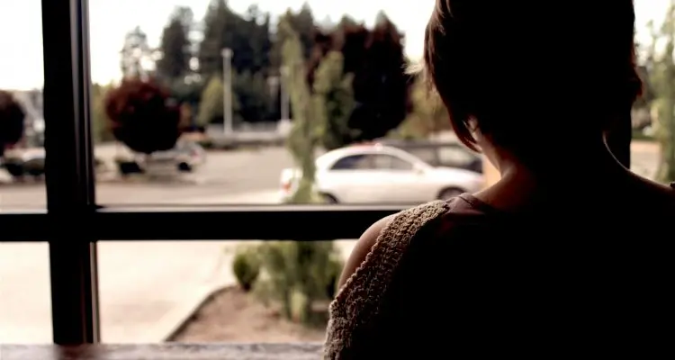 Person seen from behind beside a large window, with a car outside