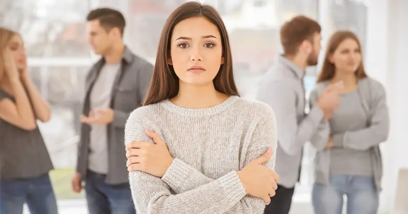 Person standing with arms folded while blurred groups talk in the background