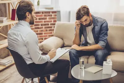 One person holds a clipboard while another sits with a hand on their forehead