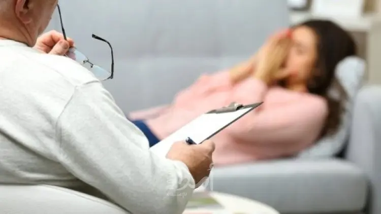 A person with a clipboard faces another person reclining on a couch