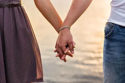 Two people holding hands outdoors beside a softly blurred shoreline