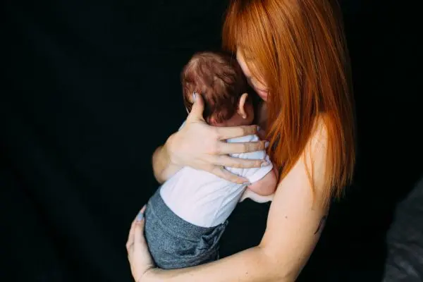 Red-haired adult holds a baby close against a black background