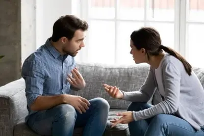 Two adults seated on a sofa, facing each other and gesturing as they talk