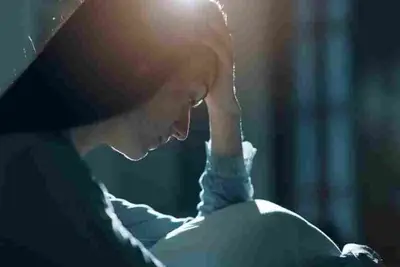 Person sits in dim light with their head lowered and held in both hands
