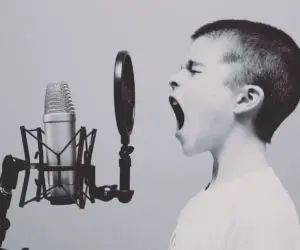 Child with mouth open facing a studio microphone and circular pop filter