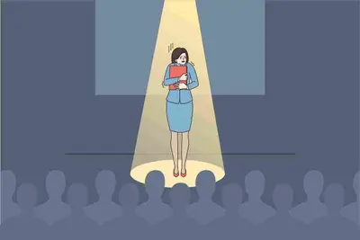 Person stands alone under a spotlight onstage before a seated audience
