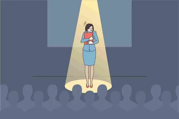 Person stands alone under a spotlight onstage before a seated audience