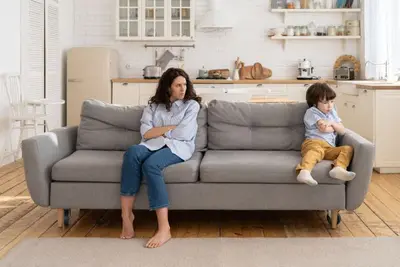 An adult and a child sit apart on a sofa with their arms crossed